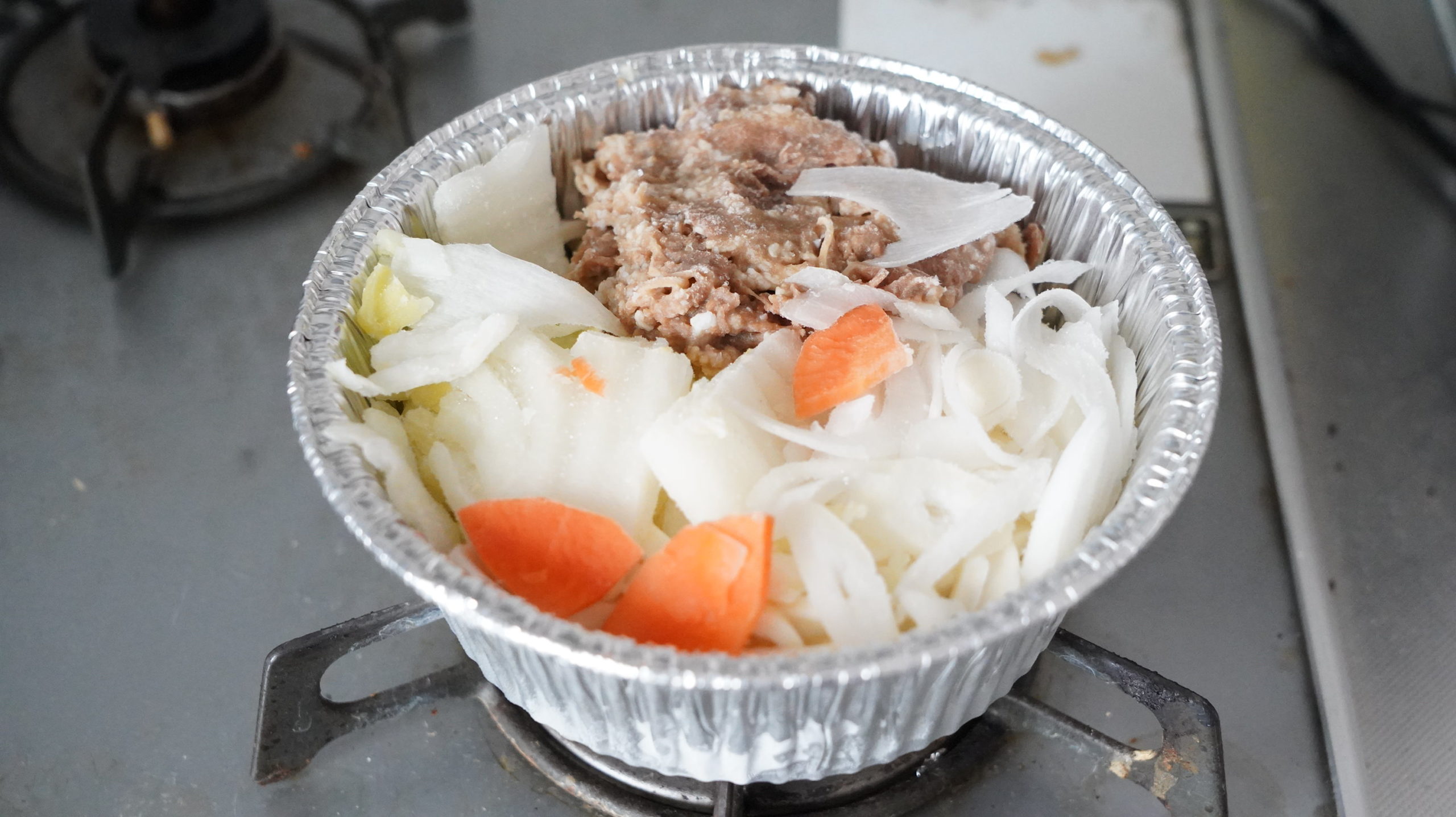 ファミリーマートの冷凍食品「牛肉の旨味！牛すき焼き鍋（うどん入り）」をガスコンロで加熱している写真