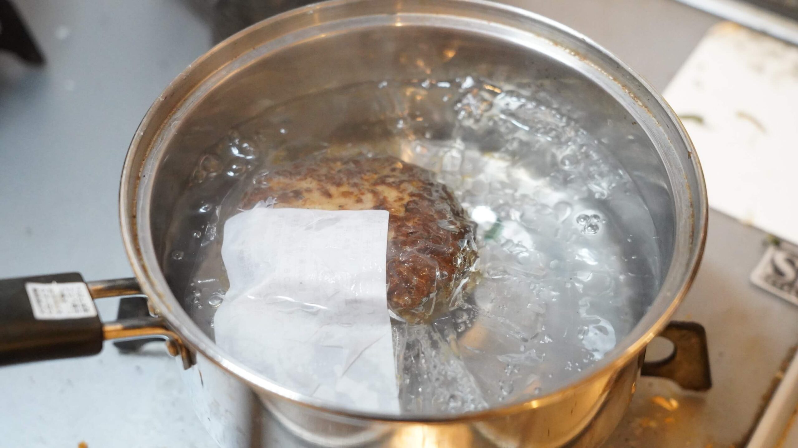 俺のフレンチの冷凍食品「ロッシーニ風ハンバーグ」を湯せんで調理している写真