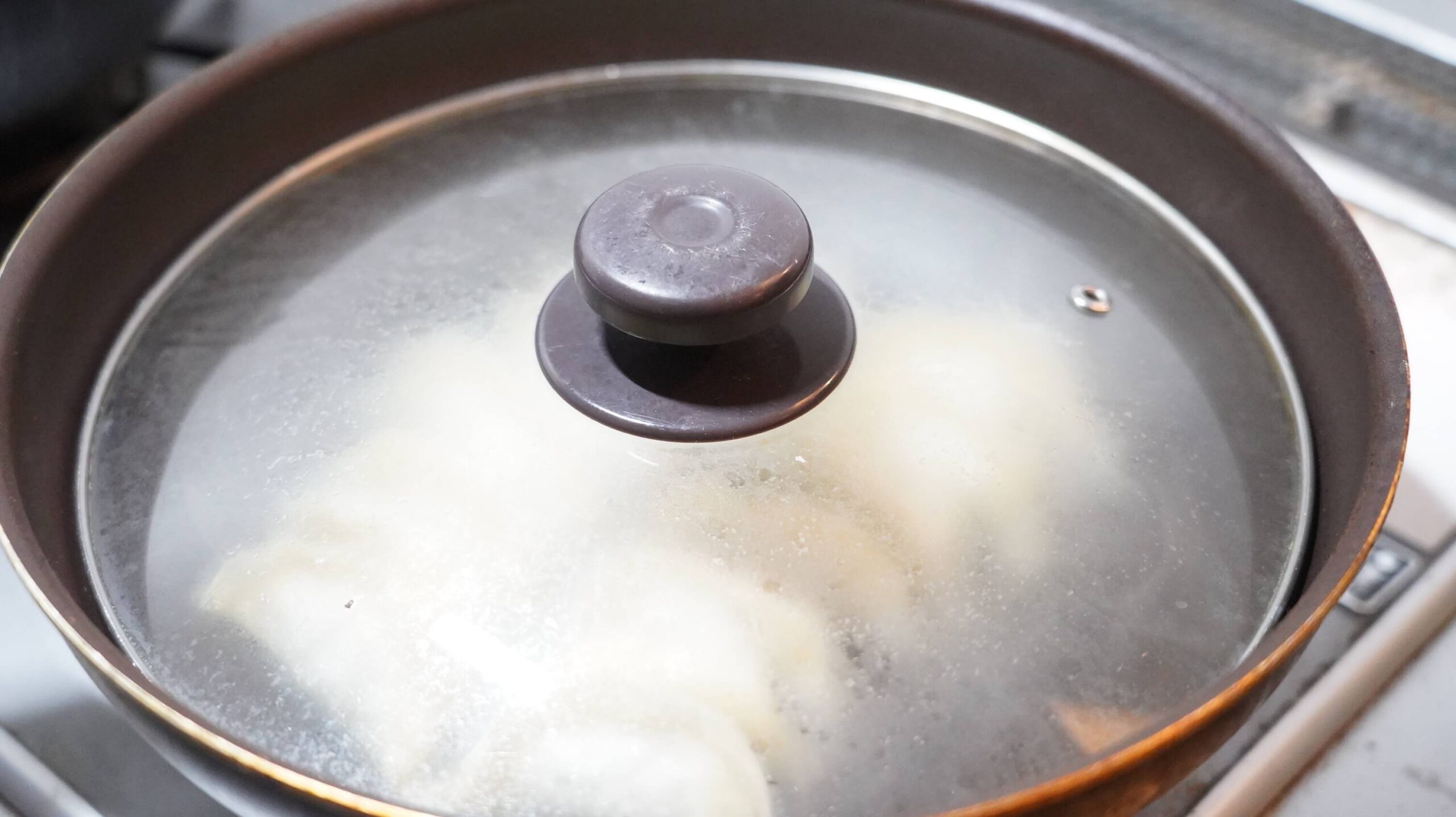 生協宅配限定の冷凍餃子「香港ギョーザ」をフライパンで蒸し焼きにしている写真
