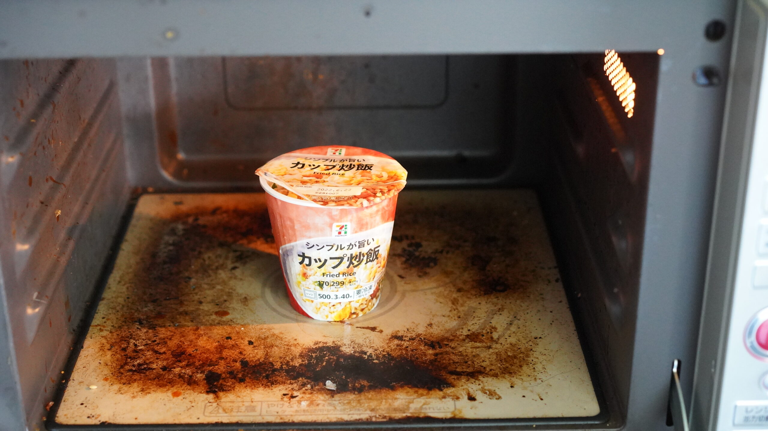 セブンイレブンのカップ型冷凍食品「シンプルで美味しい炒飯」を電子レンジで加熱している写真