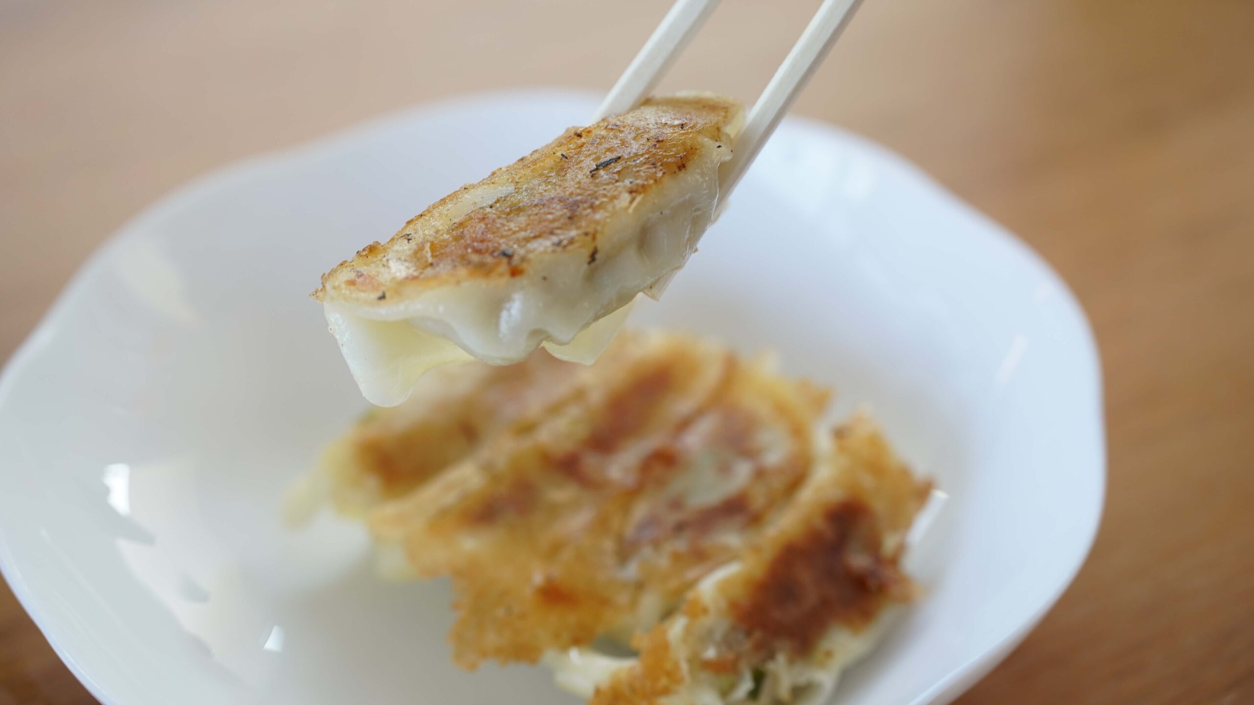 イオン・トップバリュ（TOPVALU）「ギョーザ」の冷凍食品を箸で持ち上げている写真
