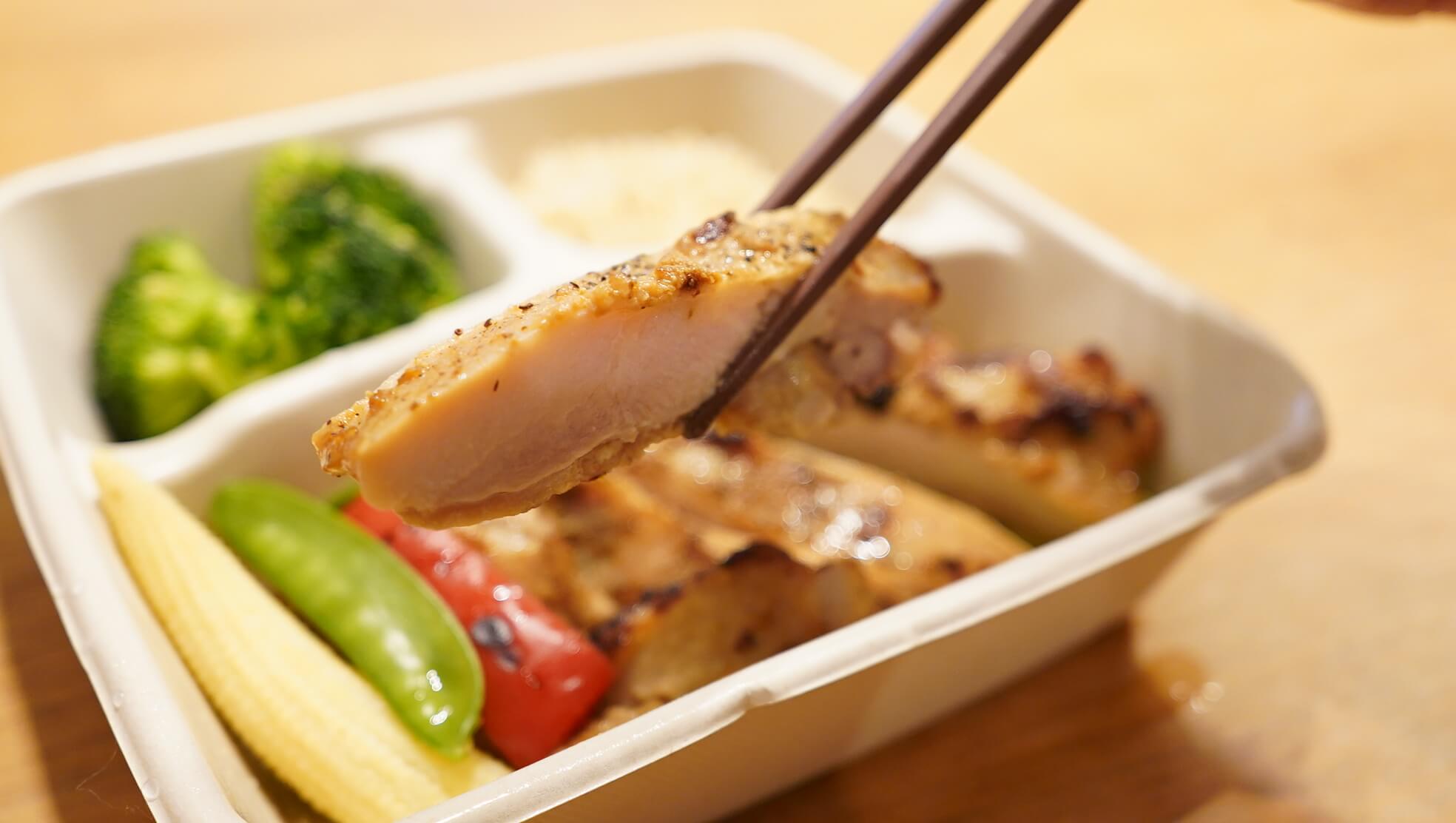 筋肉食堂DELIの「皮なし鶏モモ肉ピリ辛チキン」を箸で持ち上げている写真