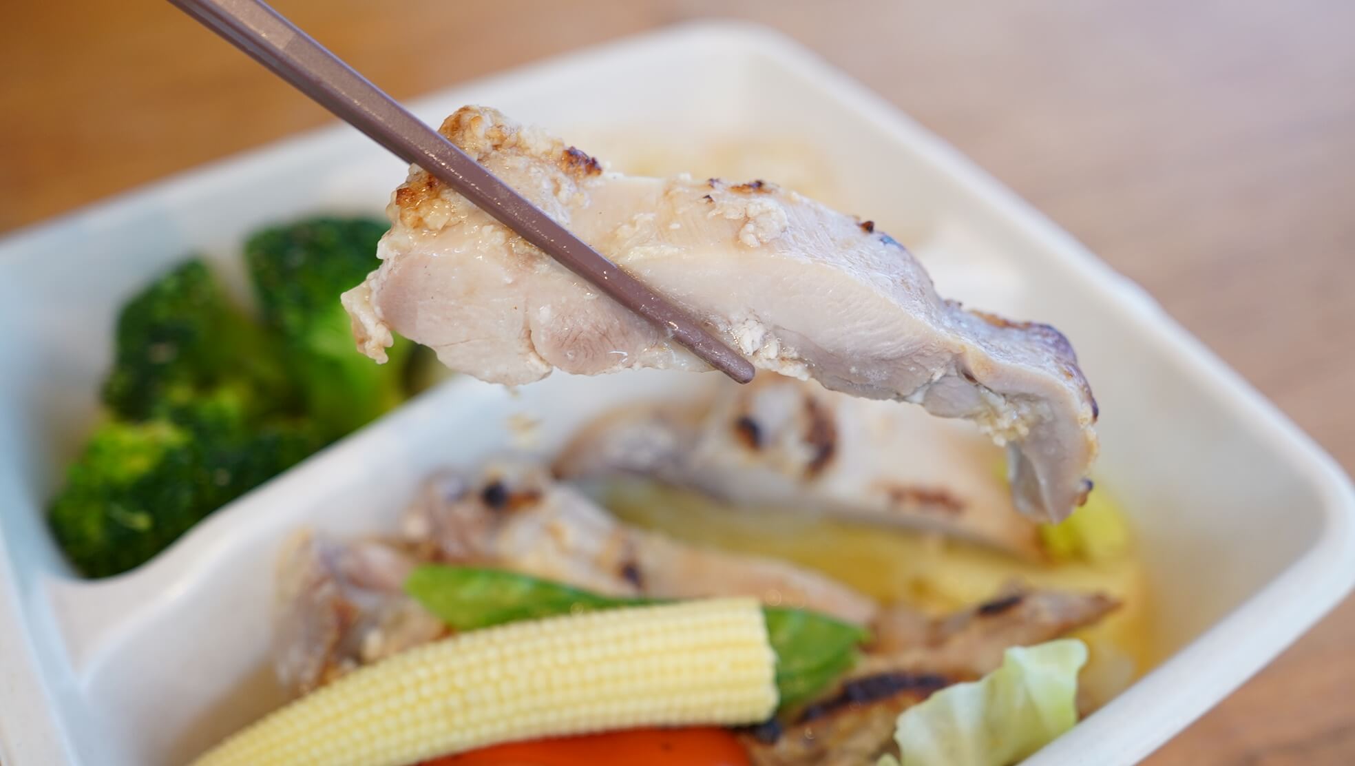 筋肉食堂DELI（冷凍宅配弁当）の「皮なし鶏モモ肉塩麹焼き」を箸で持ち上げている写真